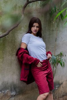 Stylish woman in casual attire posing against a textured outdoor wall.