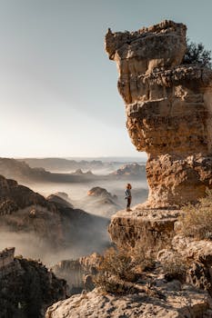 在雾天旅行时，一位匿名女性旅行者站在破旧的山侧，高耸的悬崖下，天空宁静
