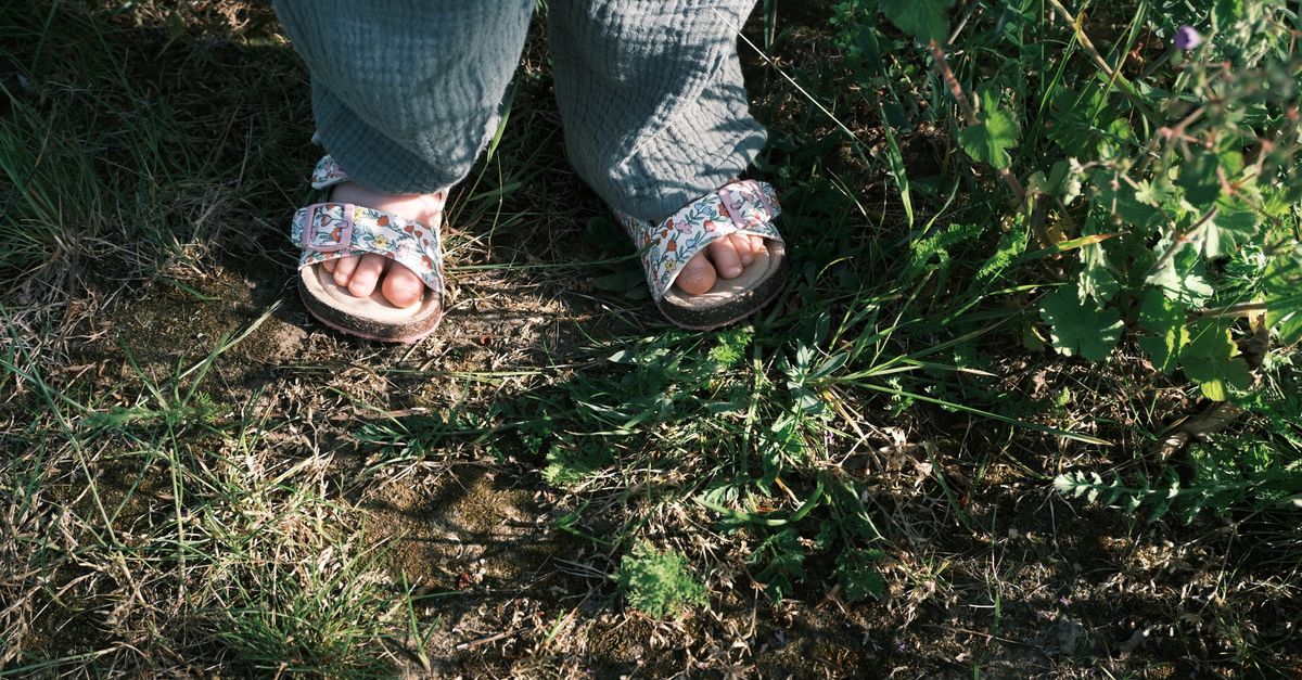 Close-up of a child's feet wearing floral sandals standing on green grass outdoors.