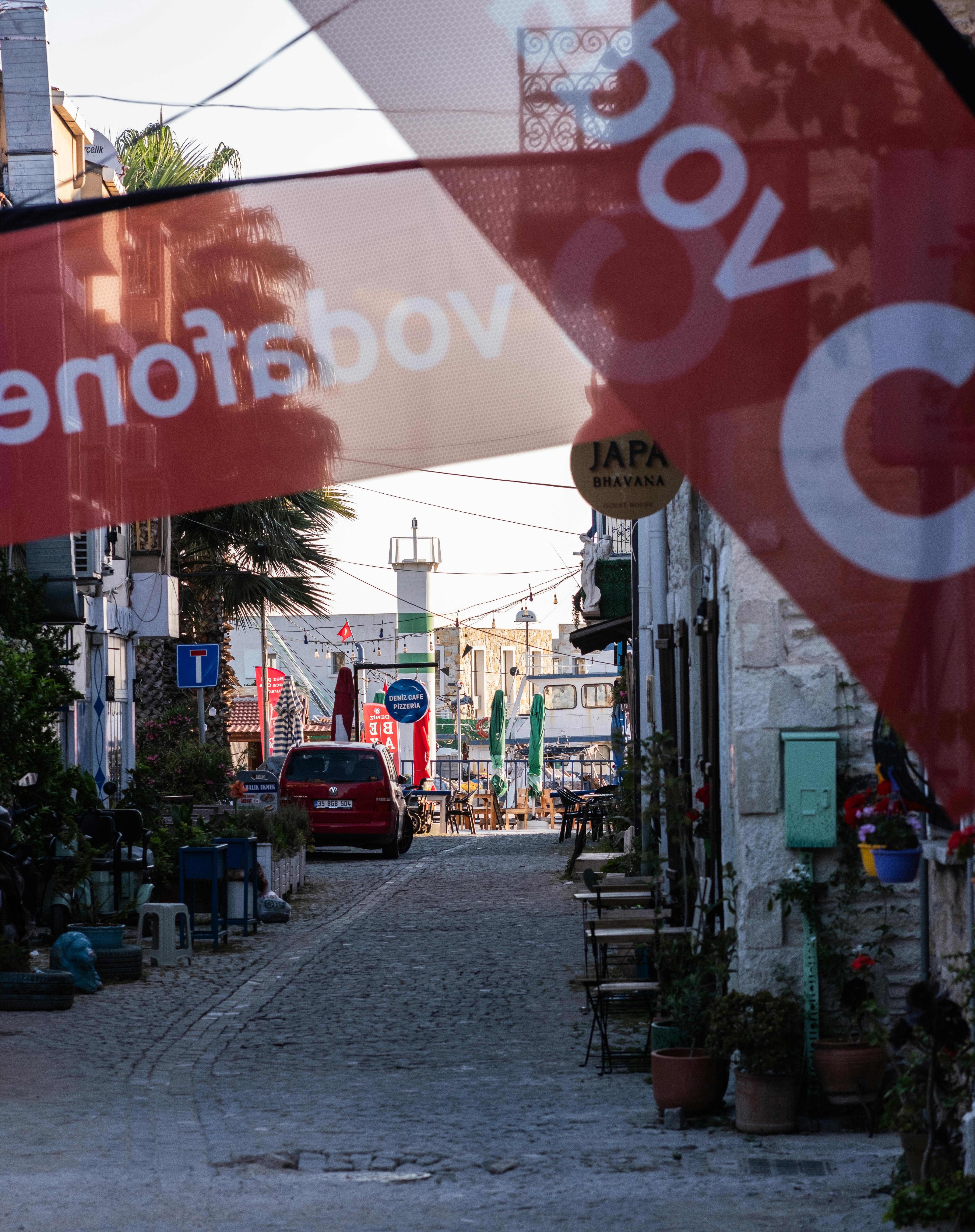 Charming cobblestone street in Foça with outdoor cafes and vibrant banners, ideal for a stroll.