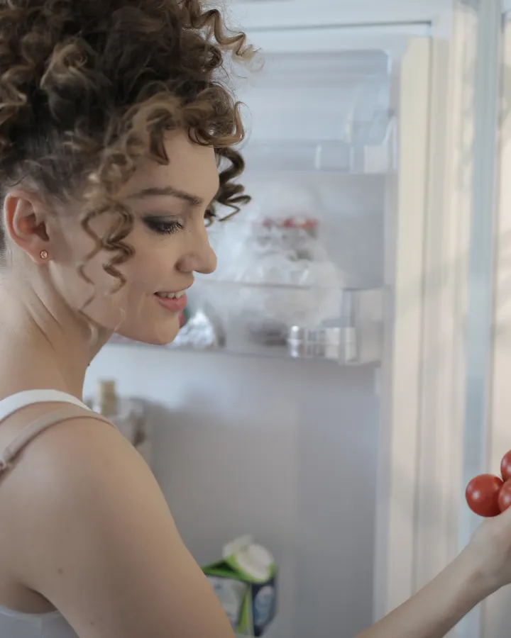 Why Does My Refrigerator Smell Bad? Causes and Fixes Smiling woman holding grapes beside an open refrigerator in a kitchen