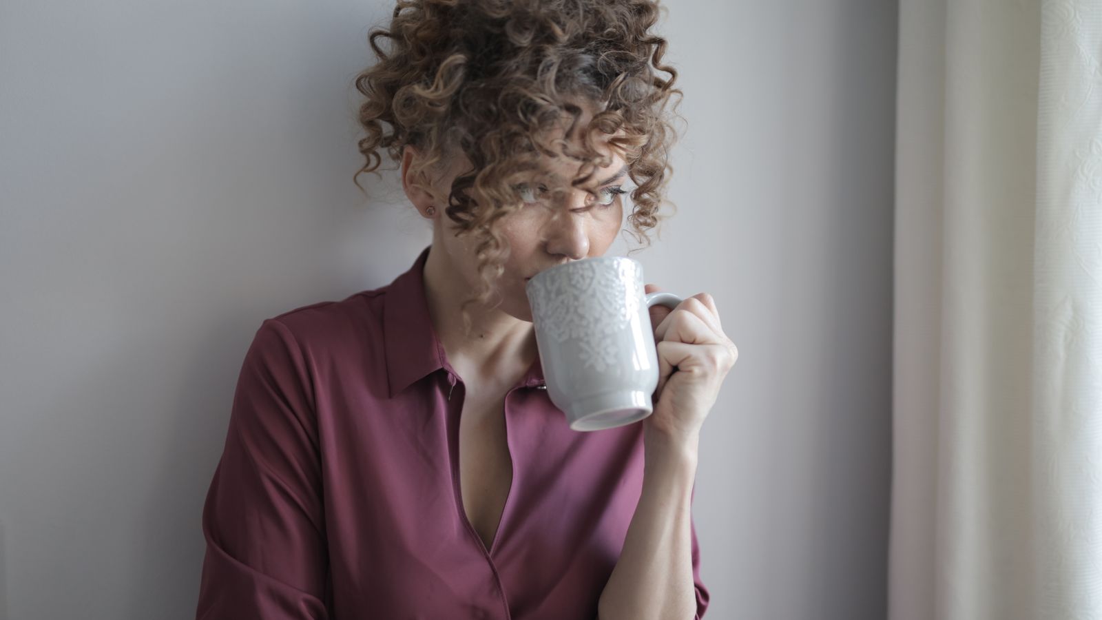 An adult holding a coffee cup near a window