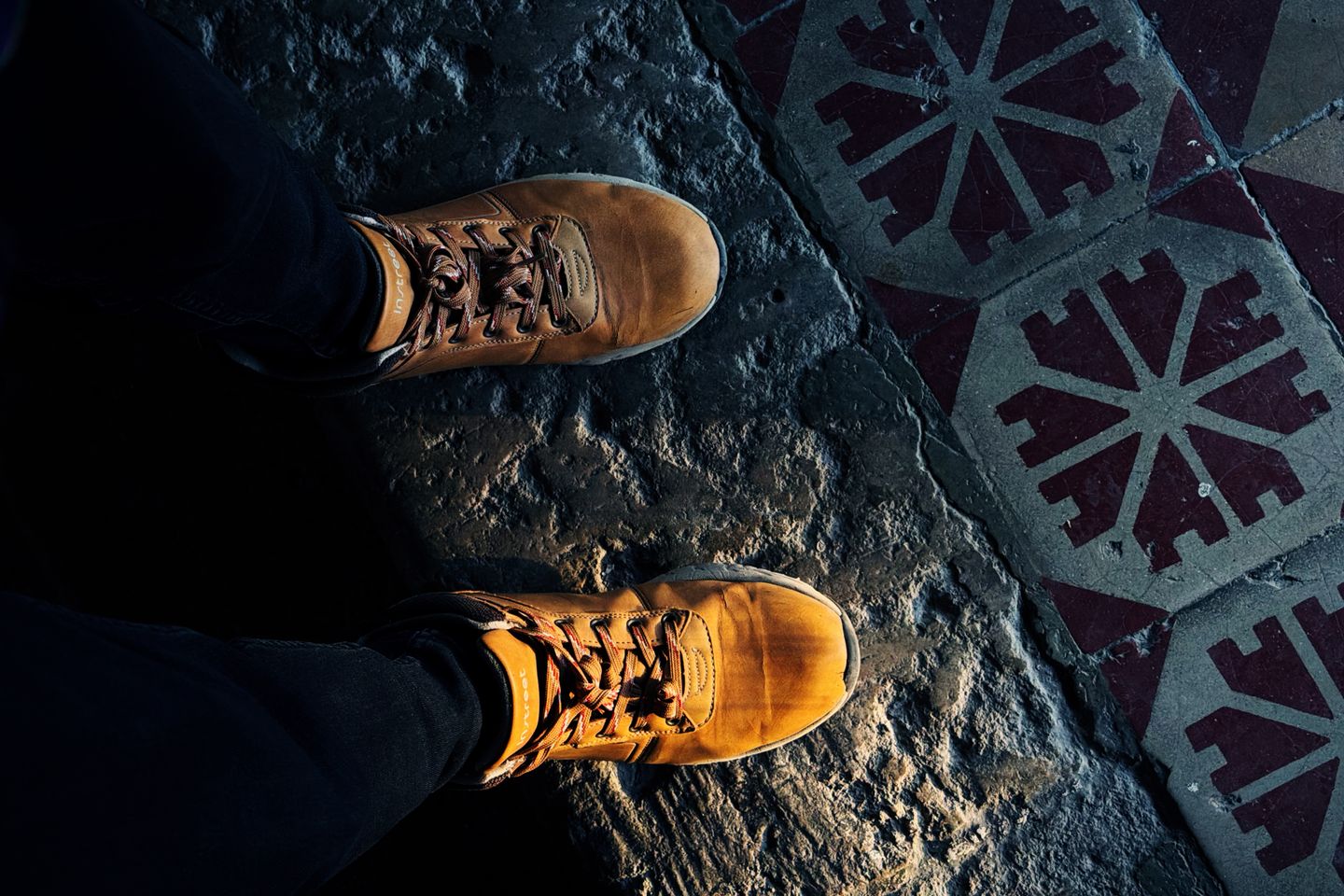A pair of tan boots on a patterned tile floor, laced and pointing hopefully at the door.