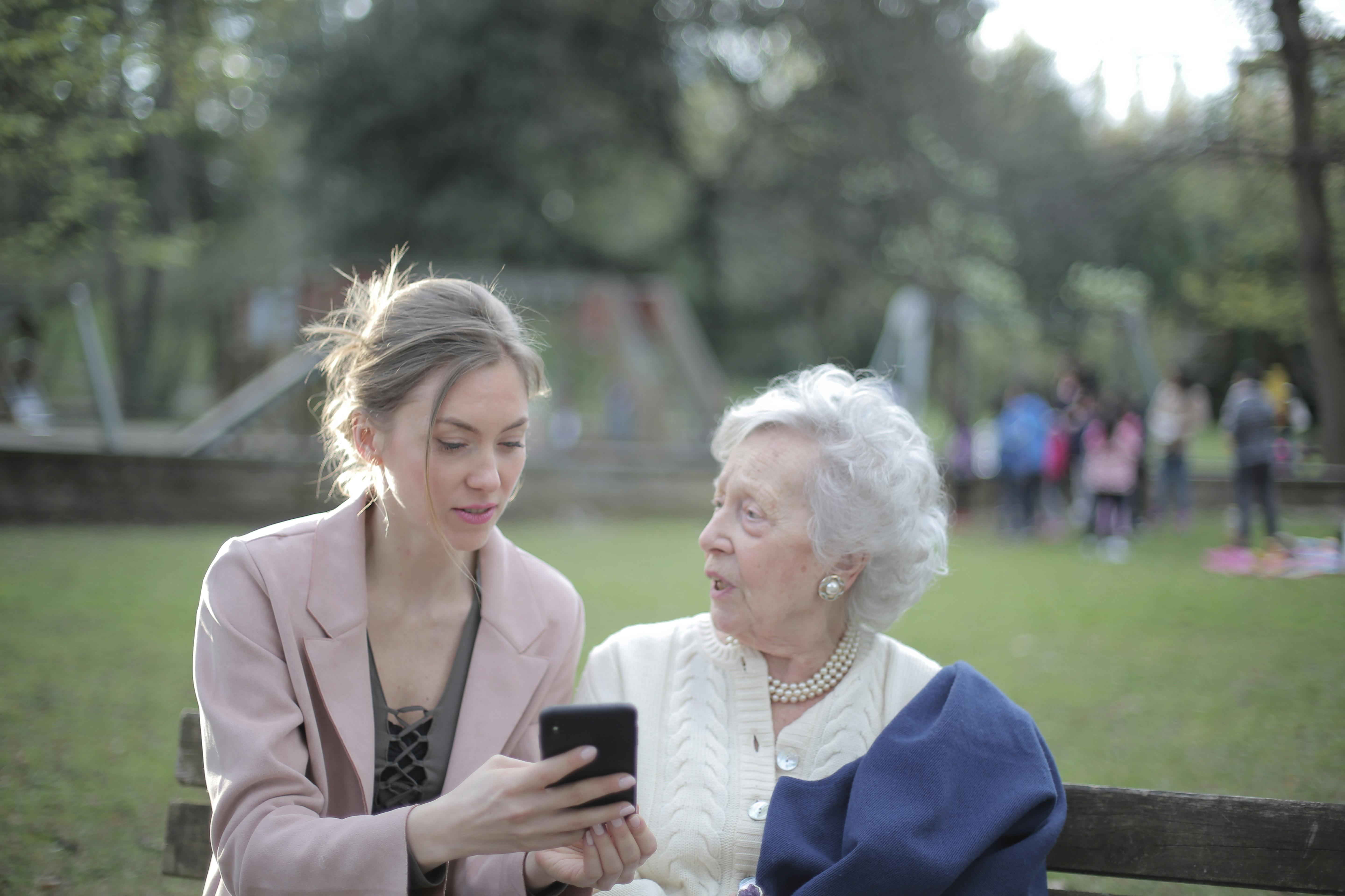 adult daughter teaching senior mother using smartphone in park