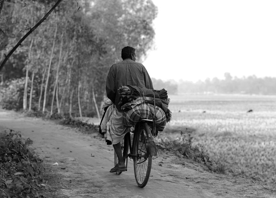 A man rides a bicycle on a rural path in Bangladesh, capturing daily life and culture.