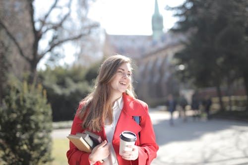 Delighted female student with takeaway coffee and books in campus