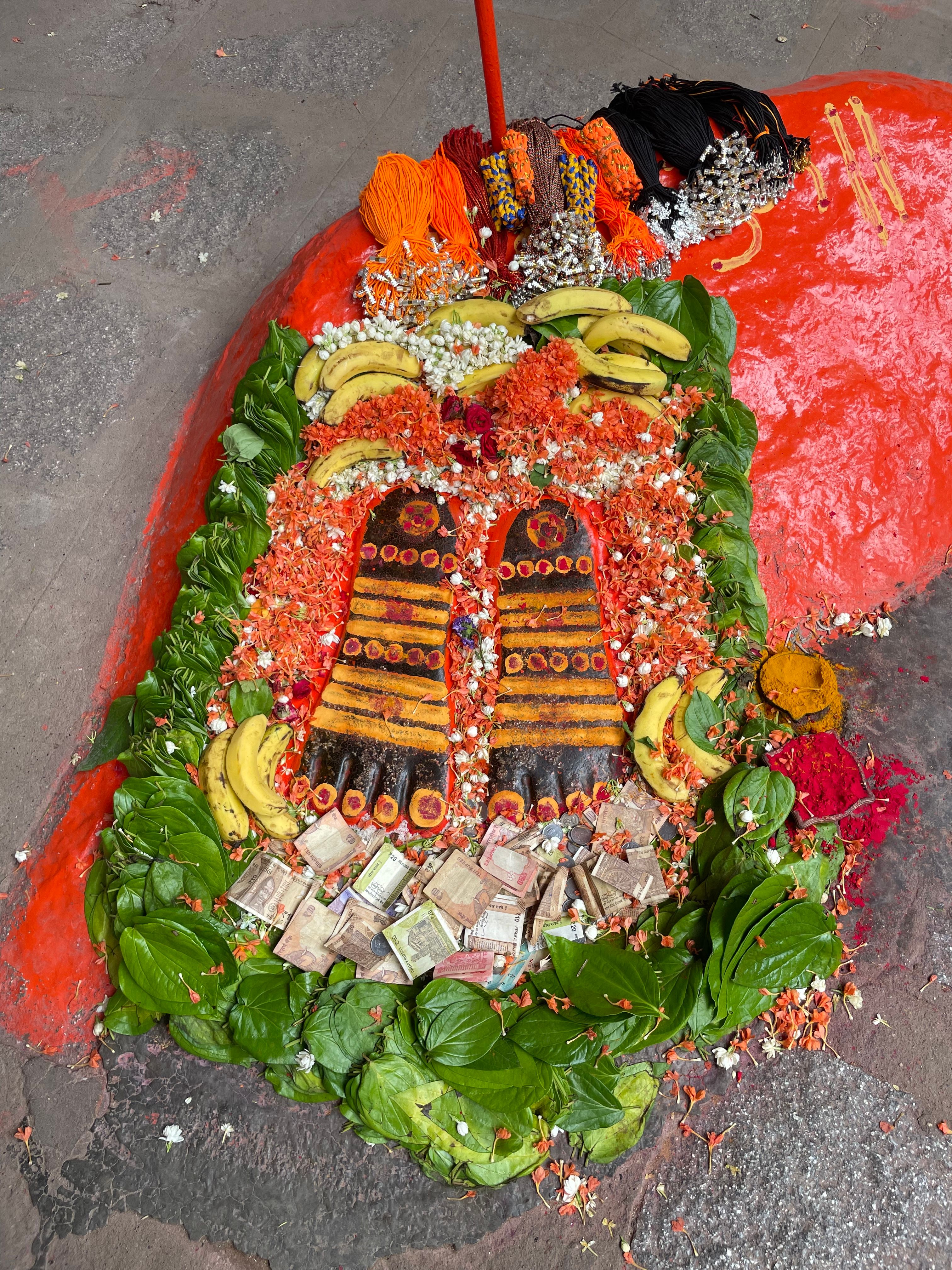 Vibrant religious offering with flowers, fruits, and coins on pavement.