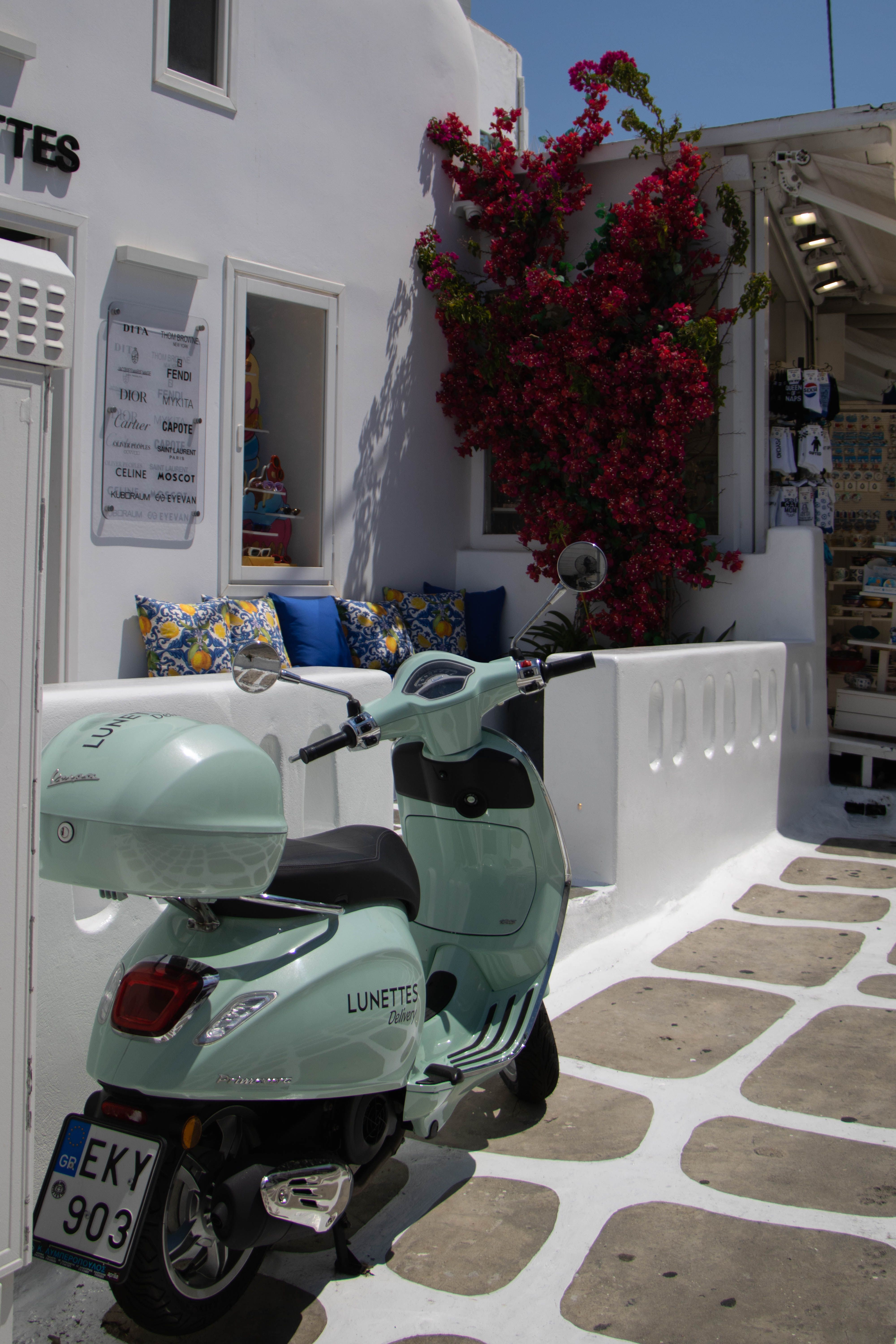 Explore the vibrant streets of Fira, Greece, featuring a pastel scooter and colorful flowers.