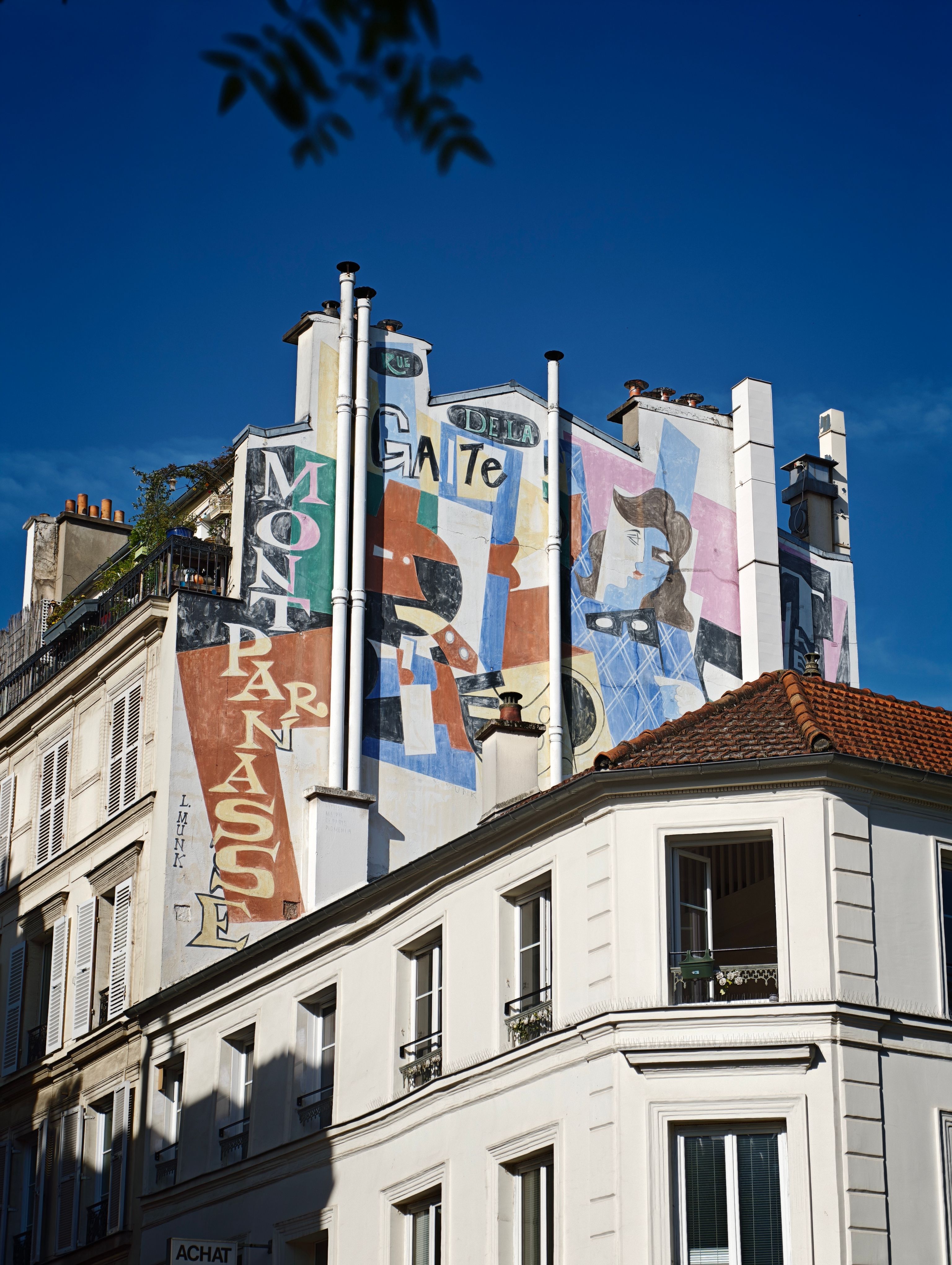 A colorful mural adorns a building in Montparnasse, Paris, under a clear blue sky.