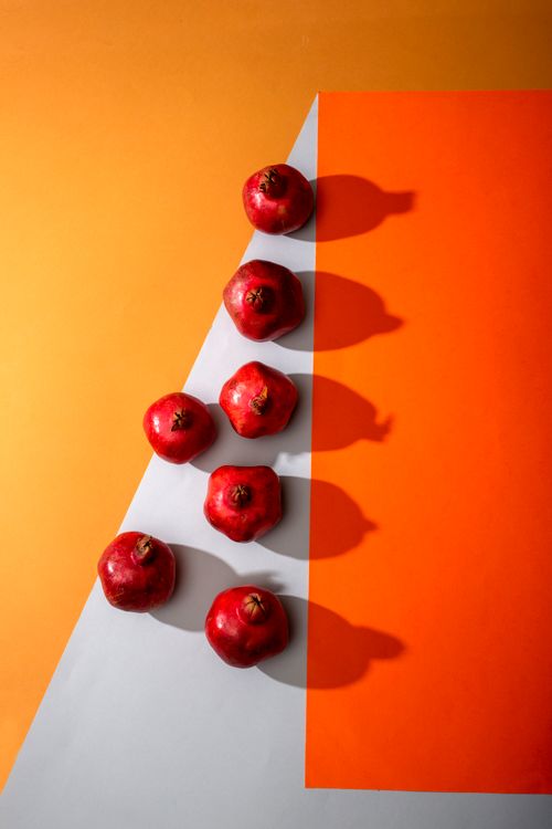 Free A creative display of red pomegranates on an orange and white surface, using dynamic lighting. Stock Photo