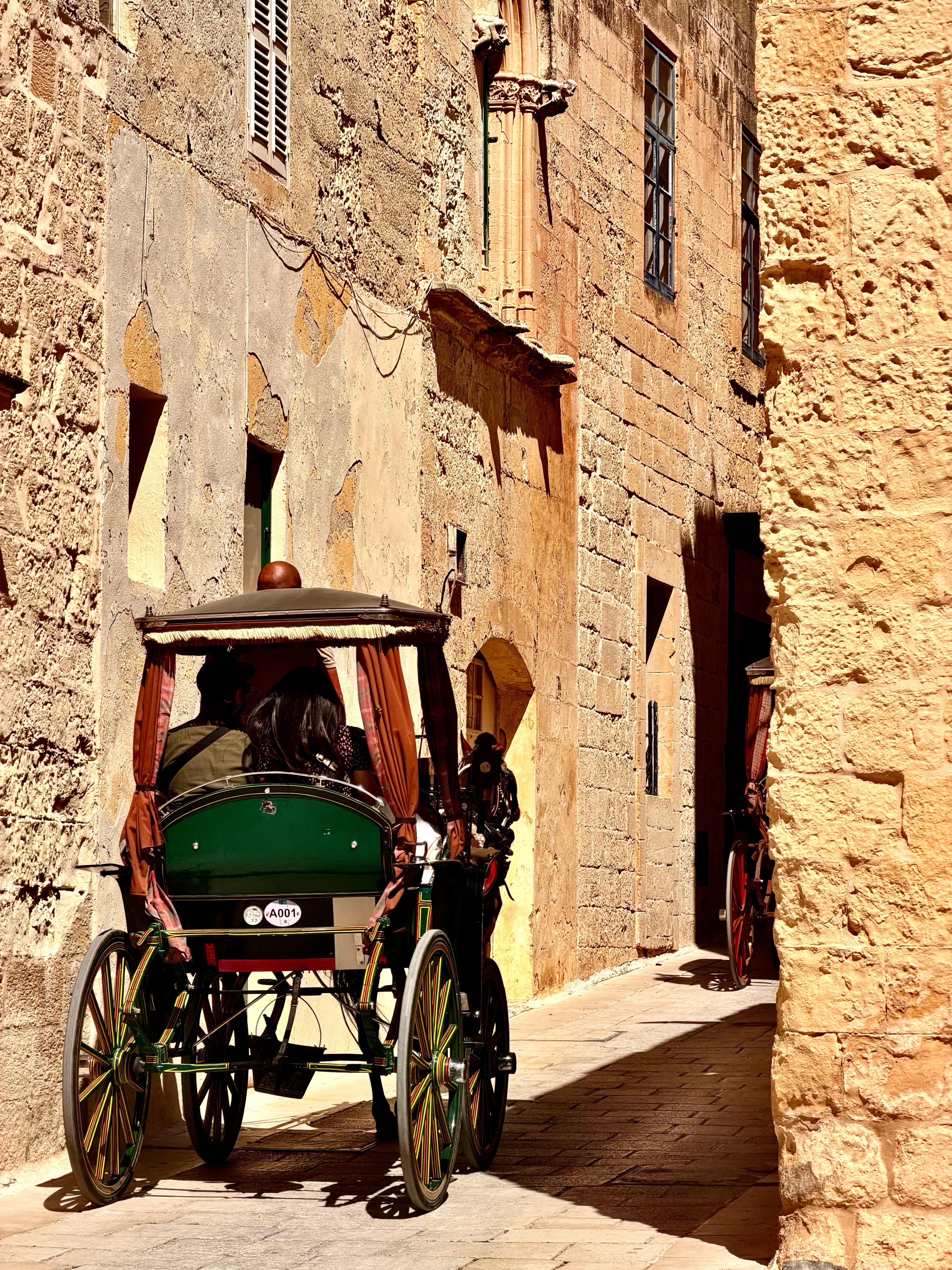 A vintage horse-drawn carriage travels down a narrow cobblestone alley in Mdina, Malta.