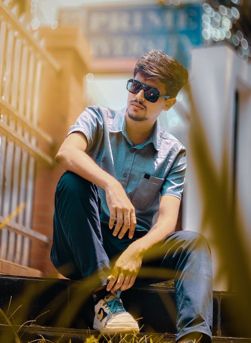 Free A stylish young man wearing sunglasses and casual attire sits on outdoor steps in Dhaka, Bangladesh. Stock Photo