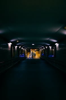 夜晚，一名匿名女性的侧影立于阴沉的现代隧道中，墙上的人造灯光照亮了隧道