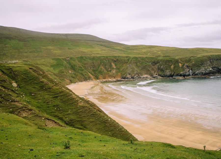 Breathtaking view of the lush green cliffs and sandy beach on Achill Island, Ireland.