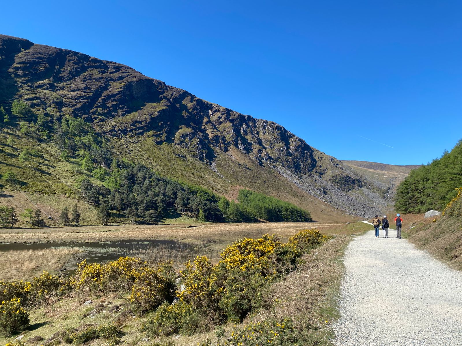 People enjoying a sunny day hike in Glendalough, Wicklow Mountains, Ireland, with mountain views