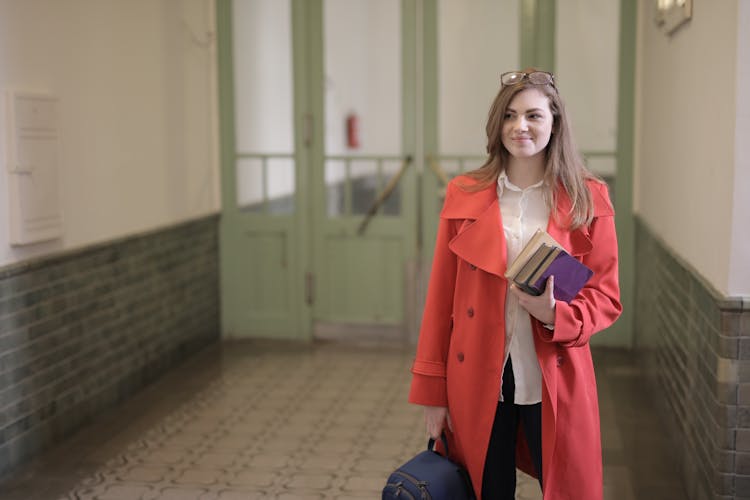 Smart Female Student With Books And Backpack In University Hallway