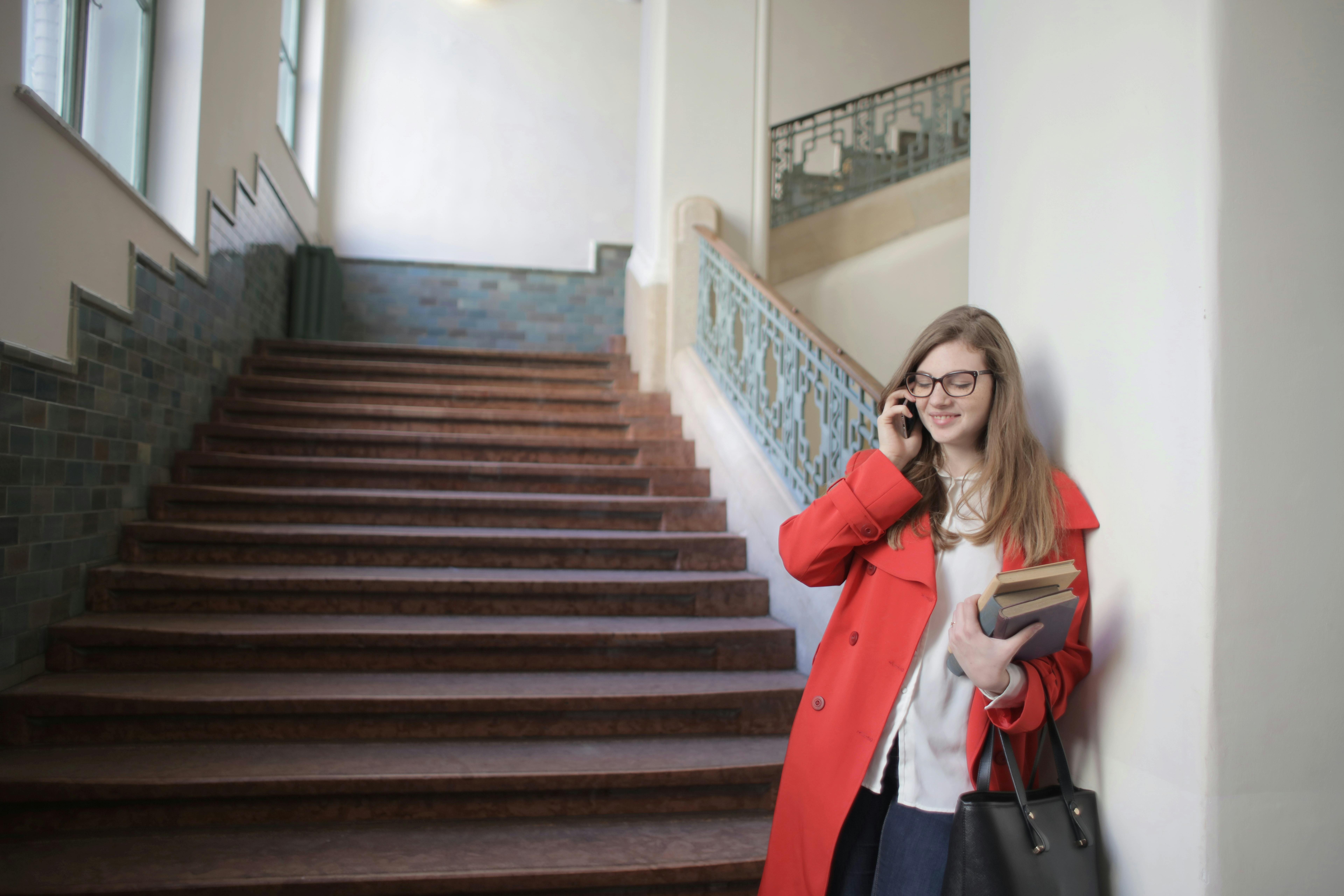 young smiling woman talking on smartphone in university near stairs