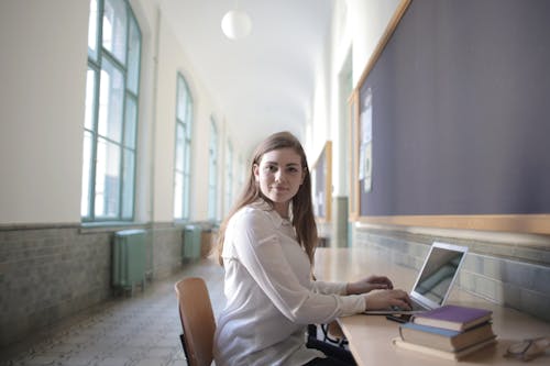 Free Female student typing on laptop in university hallway Stock Photo
