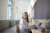 Female student typing on laptop in university hallway