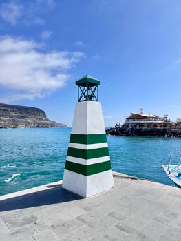 Green-striped lighthouse by the sea in Canárias, capturing a vibrant coastal scene.