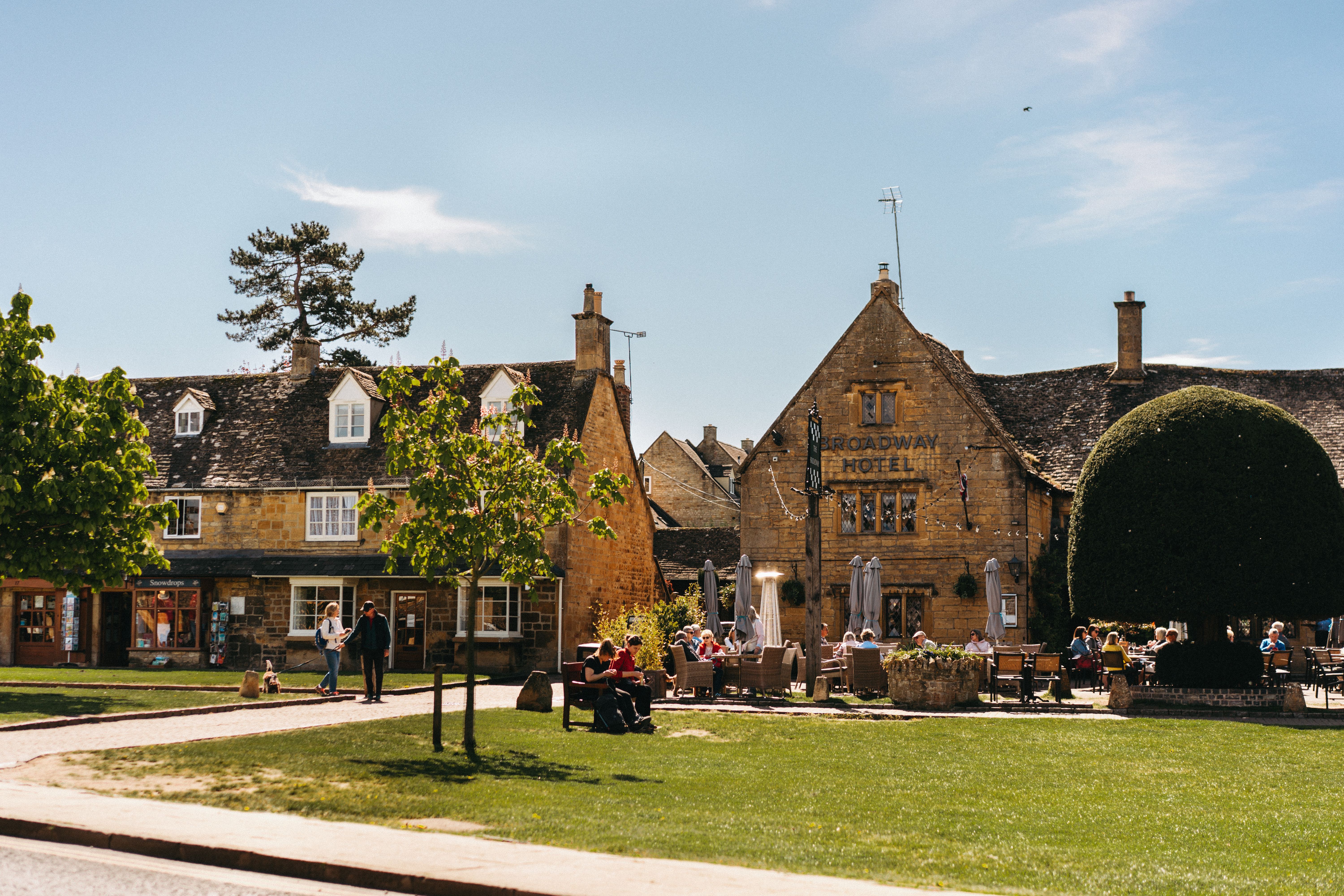 A picturesque day in a Cotswolds village featuring historic architecture and vibrant outdoor activity.