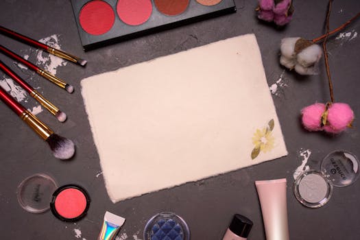 Aesthetic flat lay of makeup brushes, palettes, and cotton flowers on a dark textured surface.