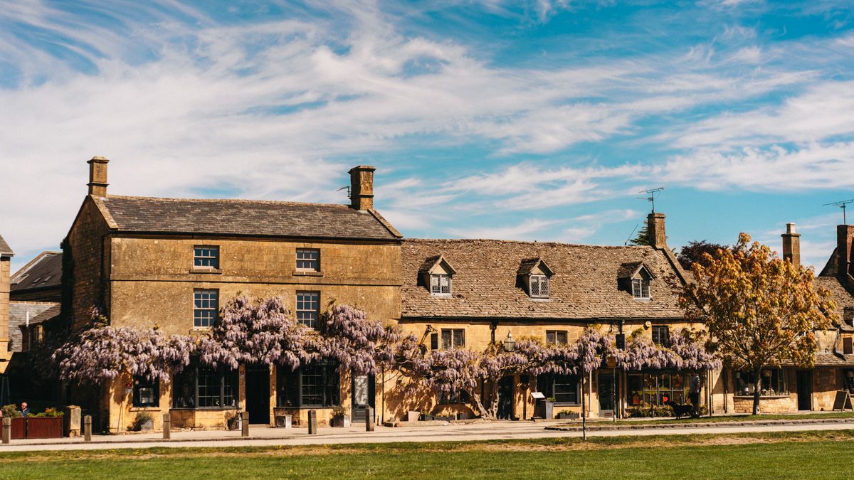 A Cotswold stone building covered in purple wisteria in spring