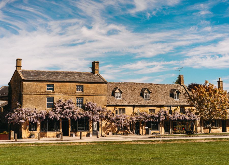 Picturesque historic building in the Cotswolds adorned with vibrant wisteria under a blue sky.