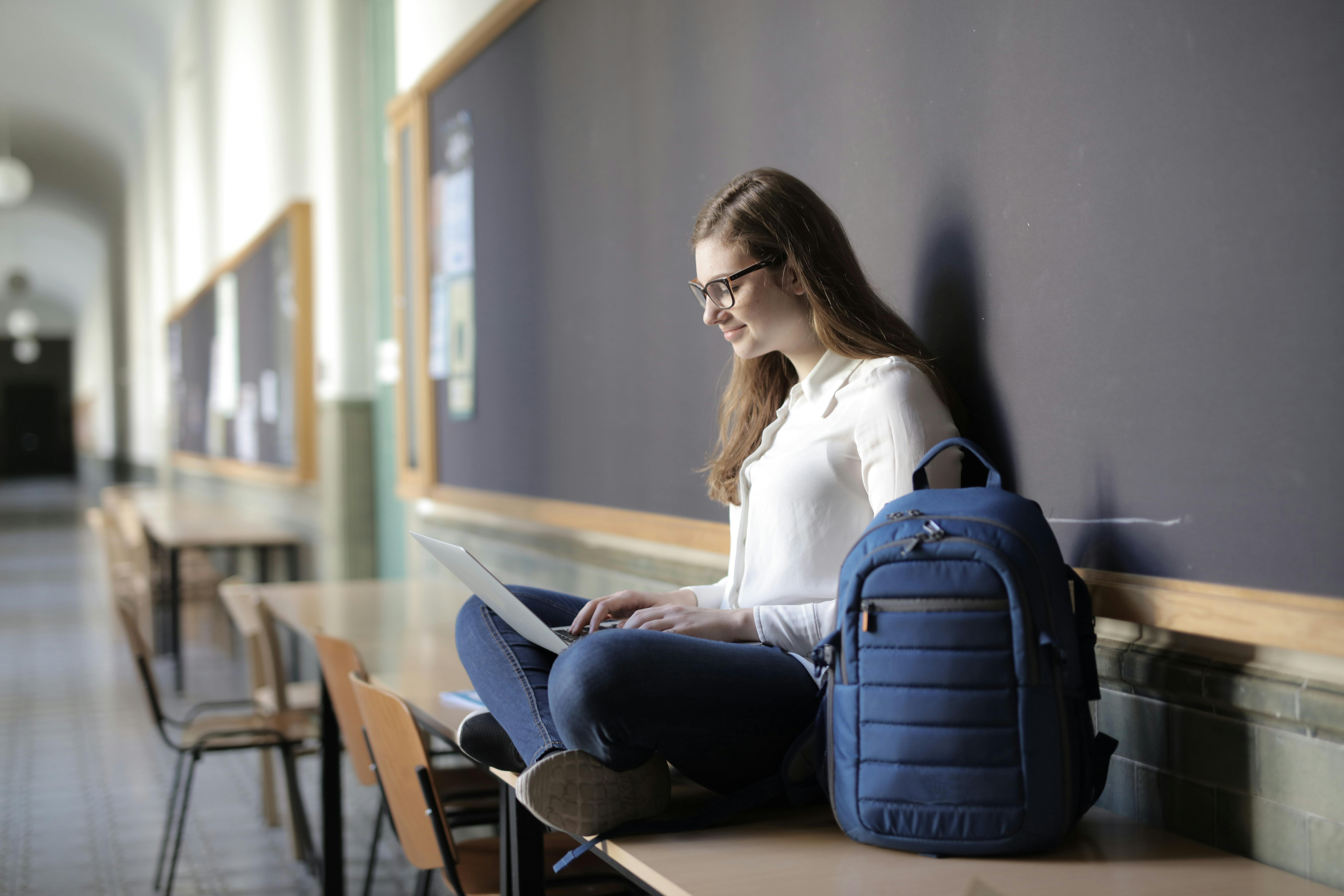 woman using laptop while sitting on table near blue backpack