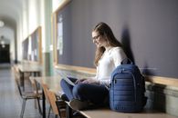 在学校走廊里，一位微笑的女人正使用笔记本电脑进行远程学习