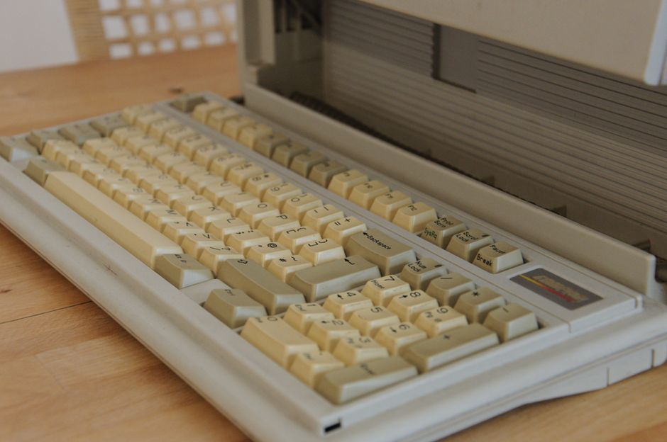 Close-up of a vintage computer keyboard with yellowed keys on a wooden desk surface.