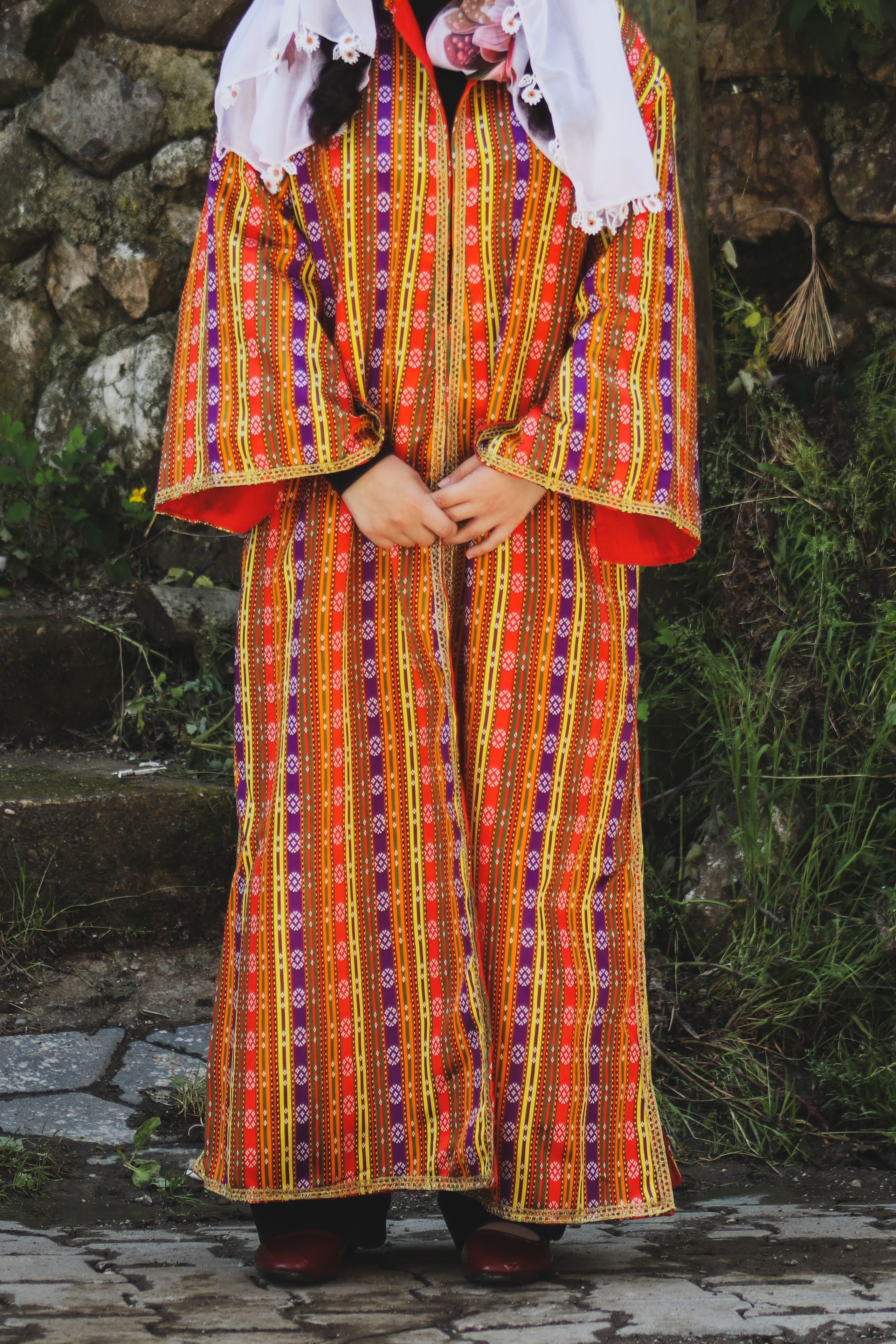 A person wearing colorful traditional attire standing outdoors on stone steps.