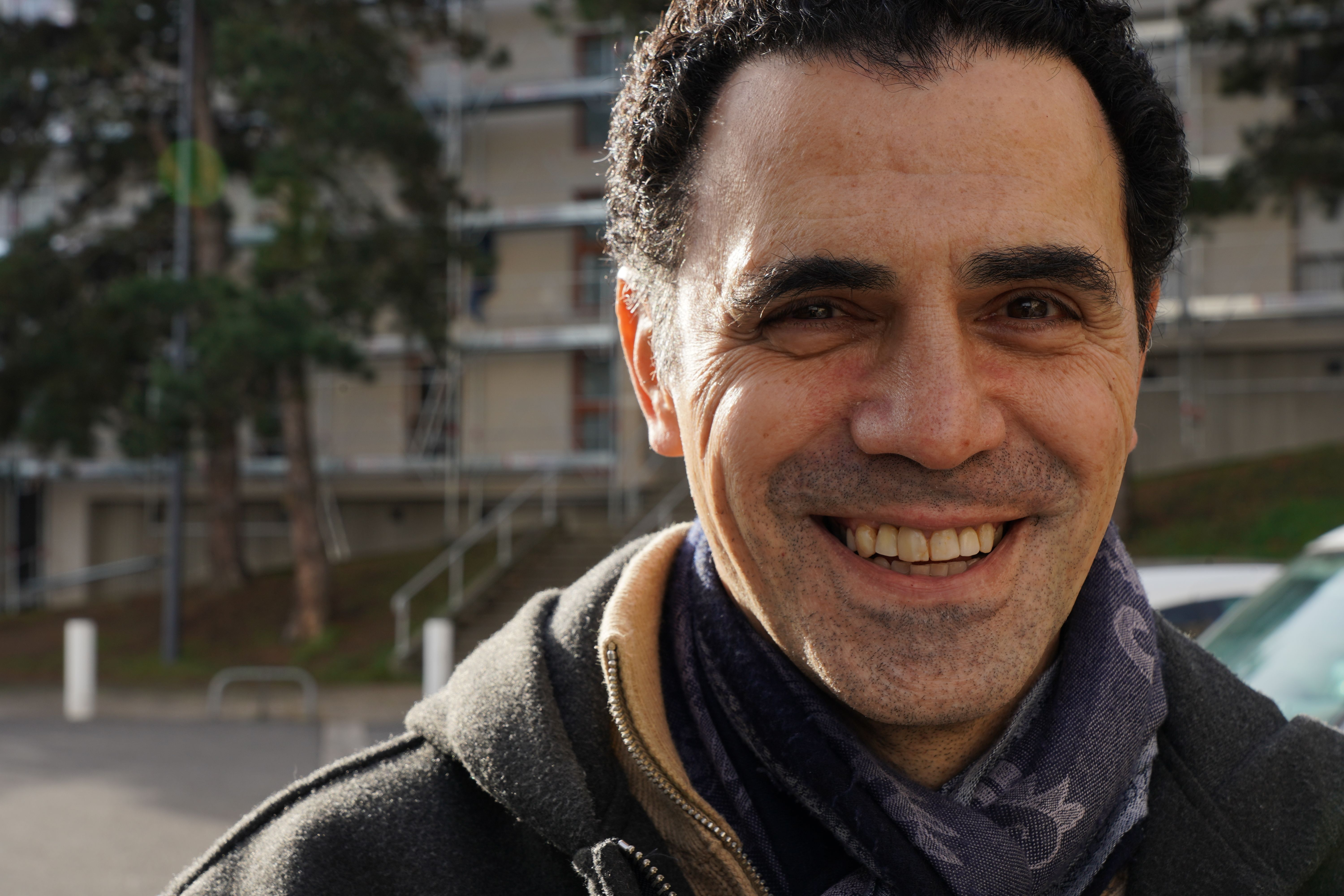 Portrait of a smiling man outdoors in Saint-Étienne, France with a residential backdrop.