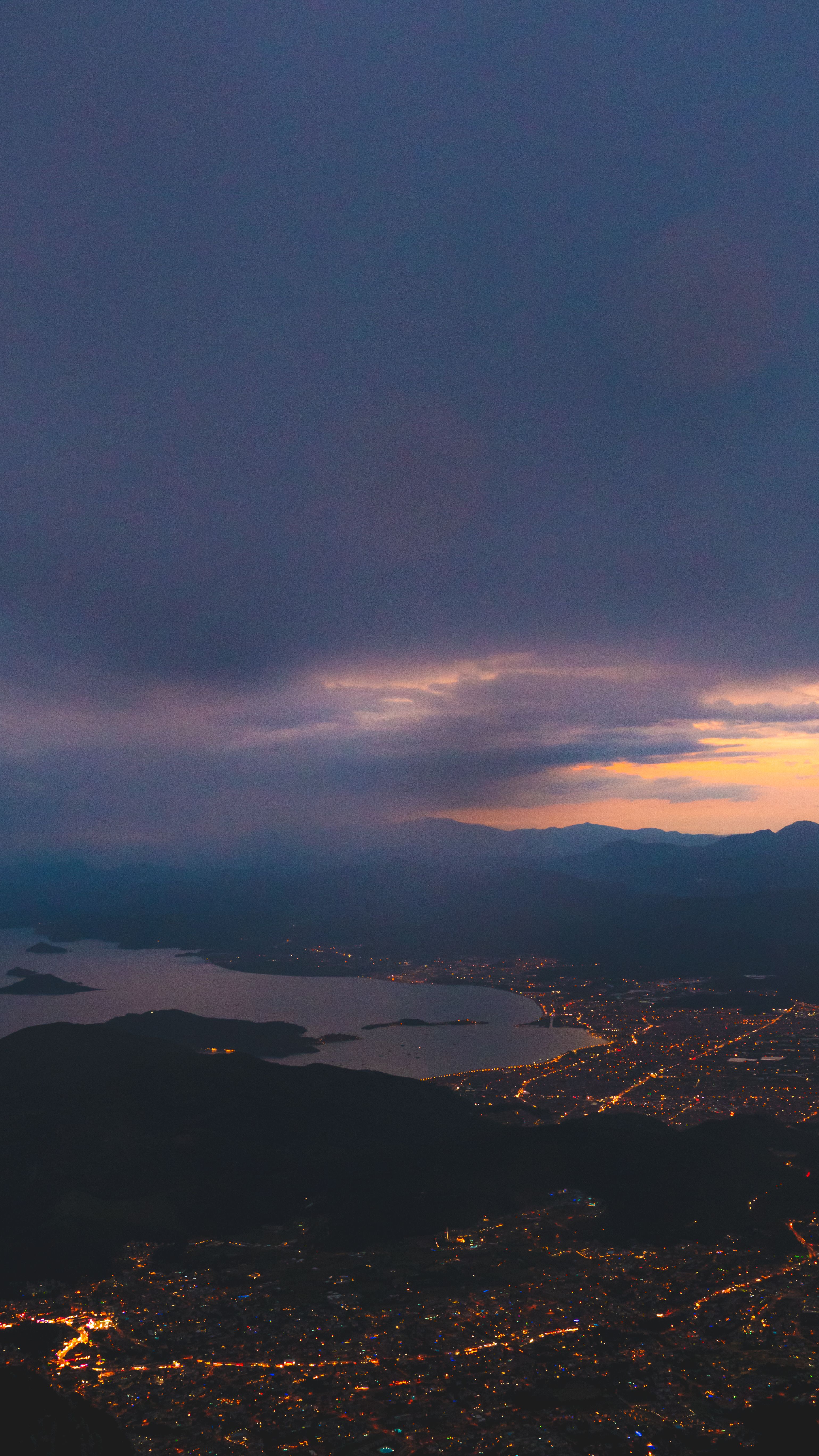 Stunning aerial view of a city illuminated at sunset over coastal landscape.