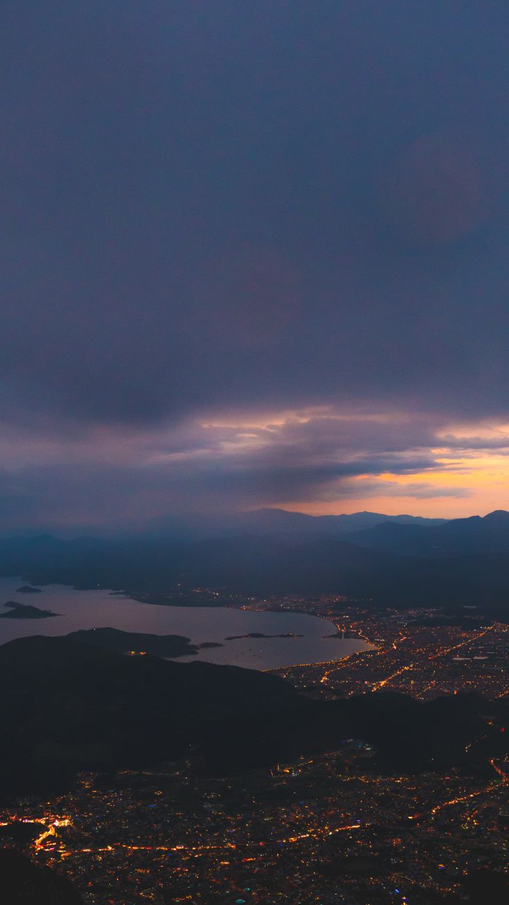 Stunning aerial view of a city illuminated at sunset over coastal landscape.