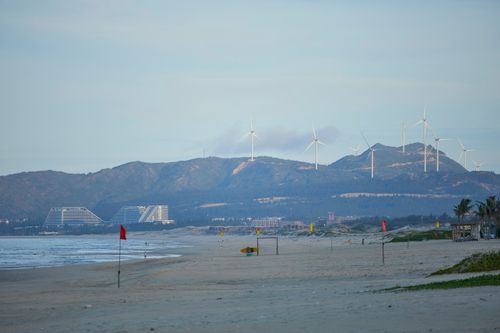 Free Tranquil beach view with wind turbines and distant mountains in Quy Nhon, Vietnam. Stock Photo