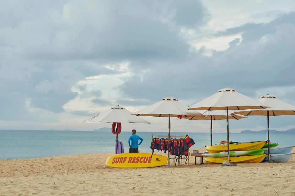 Lifeguard station on a sandy beach with surf rescue equipment, umbrellas, and kayaks under cloudy skies in Quy Nhon, Vietnam.