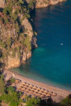 A stunning aerial capture of a tranquil beach with rocky cliffs and sun loungers along the shore.
