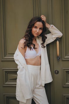 一位身穿别致白衣的年轻女子自信地倚在时尚的门边，展现着现代时尚感