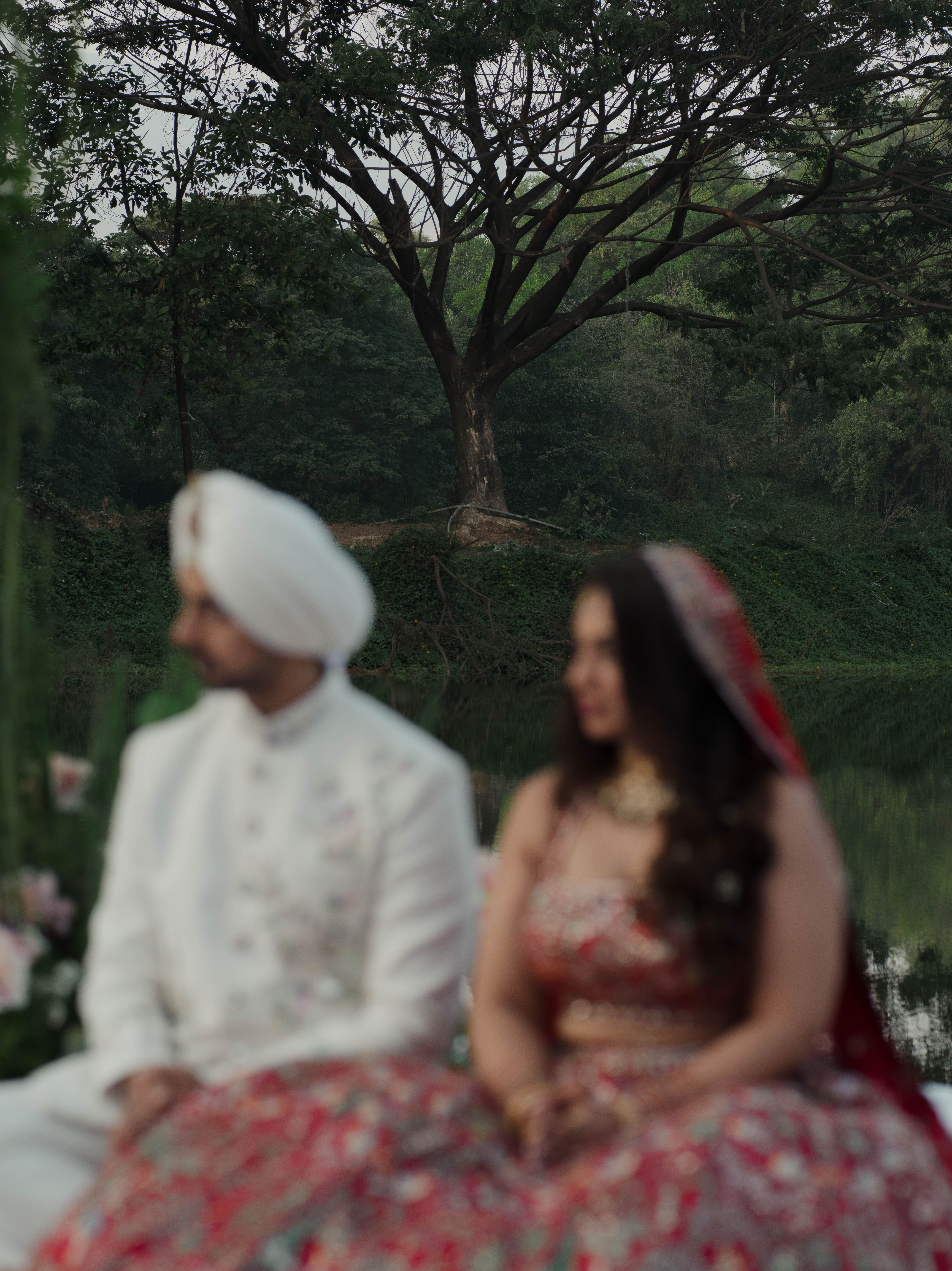 Blurred couple in traditional Indian wedding attire outdoors by a tree.