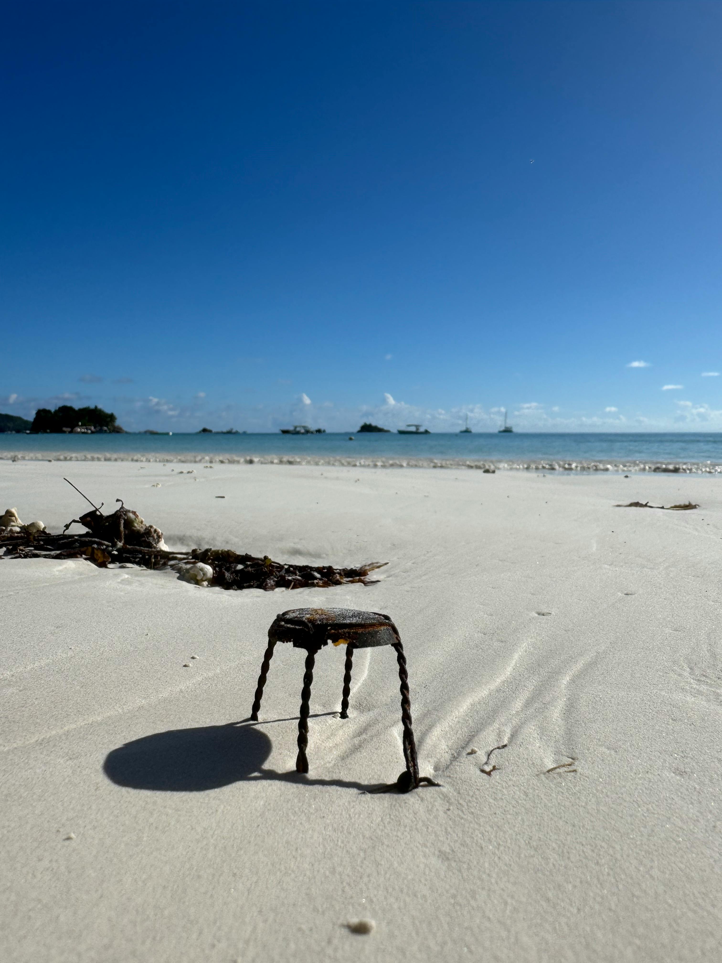 Old metal anchor in Seychelles sand under clear blue sky, capturing a serene coastal vibe.