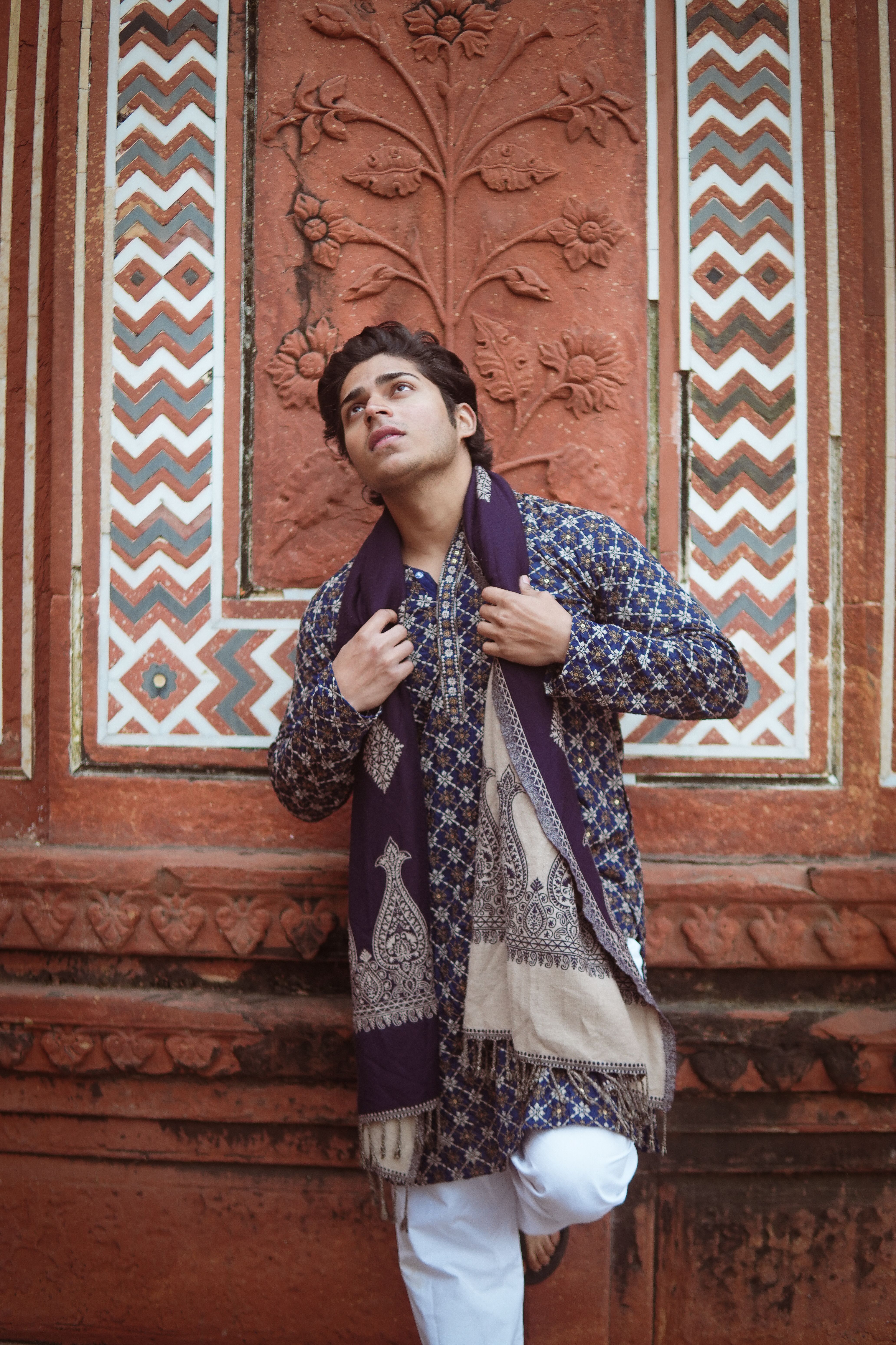 Young man in traditional Indian attire posing by intricate wall design in Agra, India.