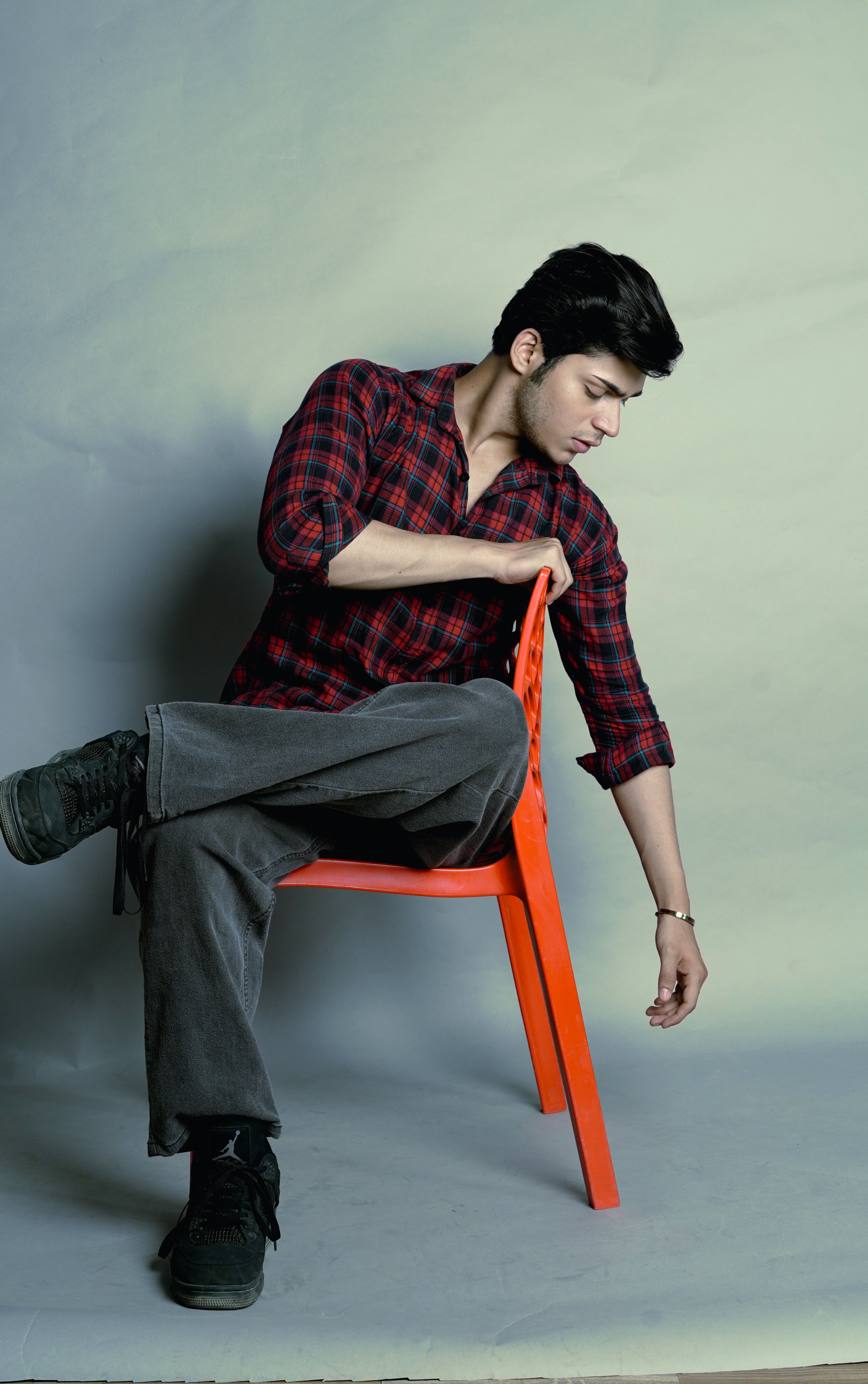 Portrait of a young man in a casual outfit sitting on an orange chair against a neutral backdrop.