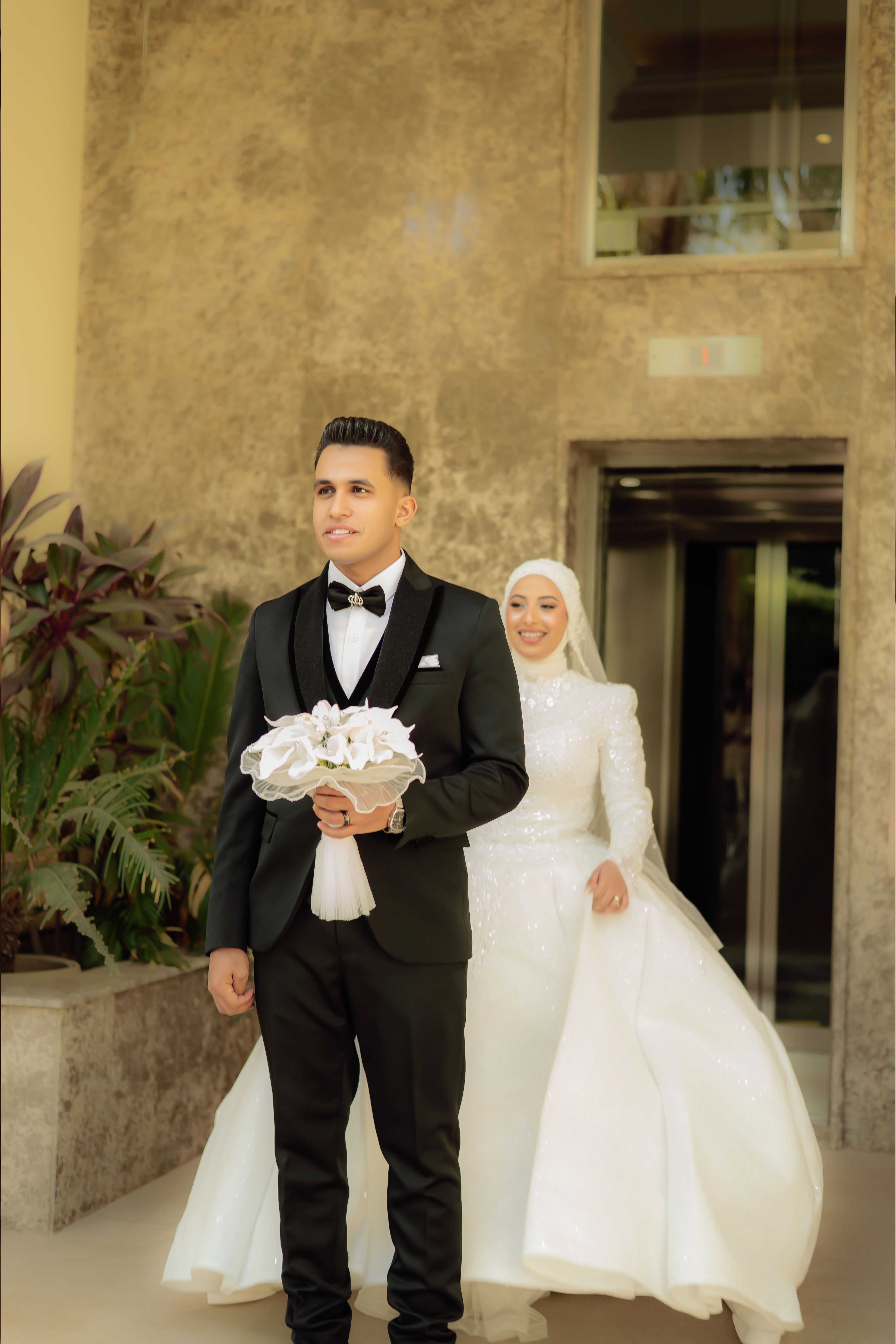 A graceful bride and groom pose outdoors, showcasing elegant wedding attire and joyful expressions.