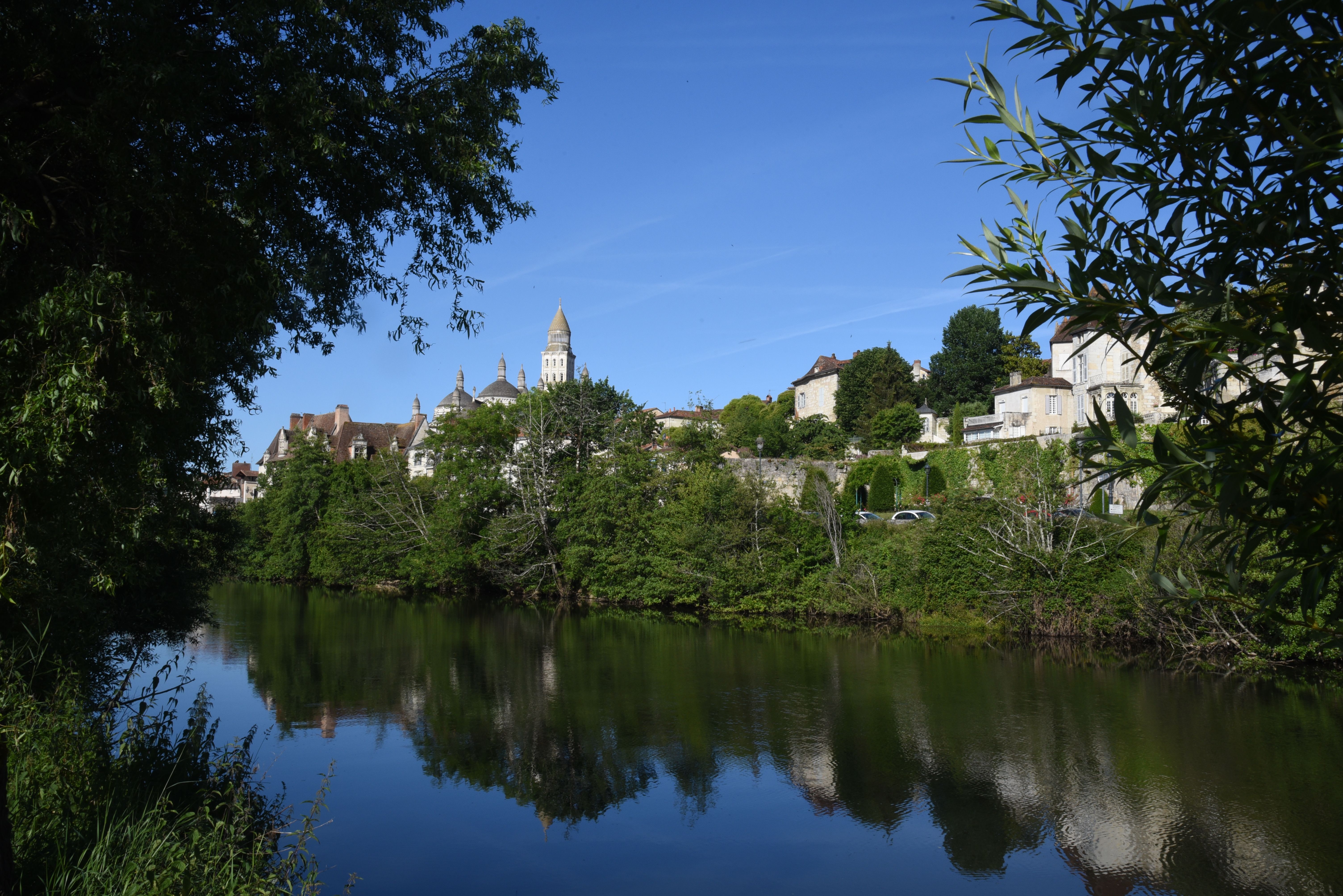 Charming riverside scene featuring a historic French town with lush greenery.