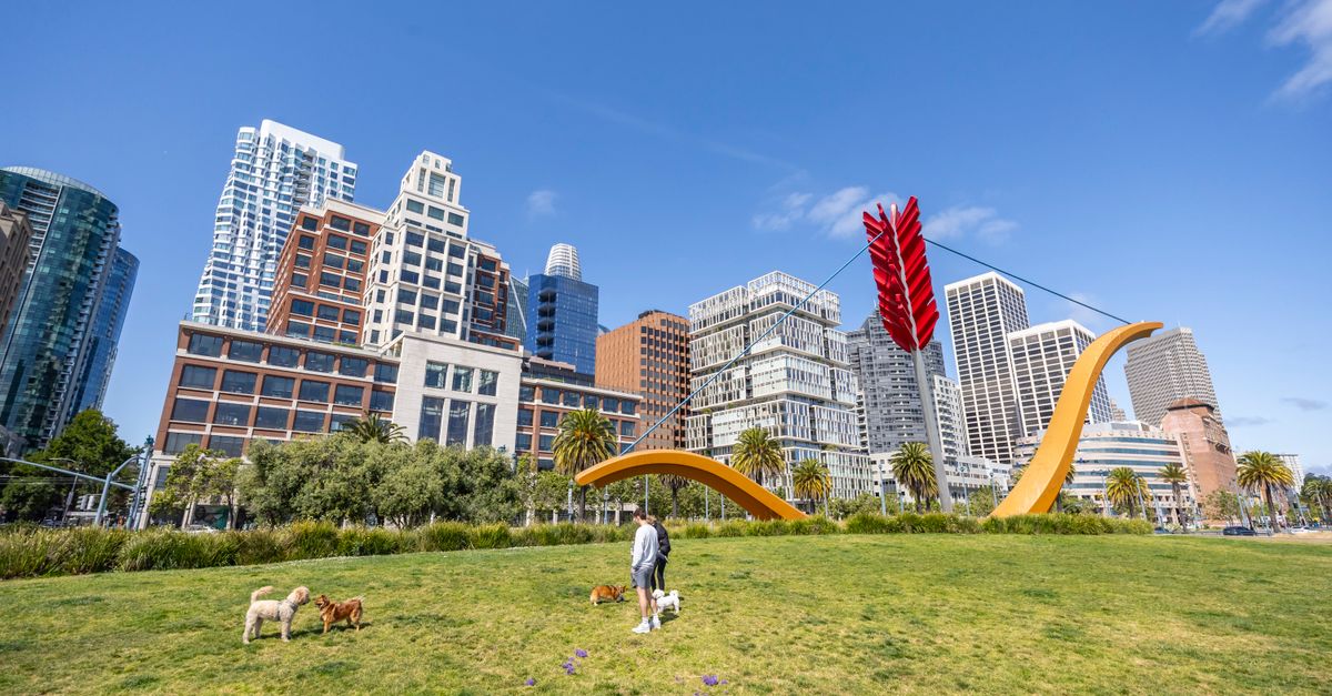 A vibrant urban park scene with a landmark sculpture, dogs playing, and city skyline.