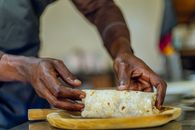 Close-up of hands preparing a fresh burrito on a wooden cutting board.