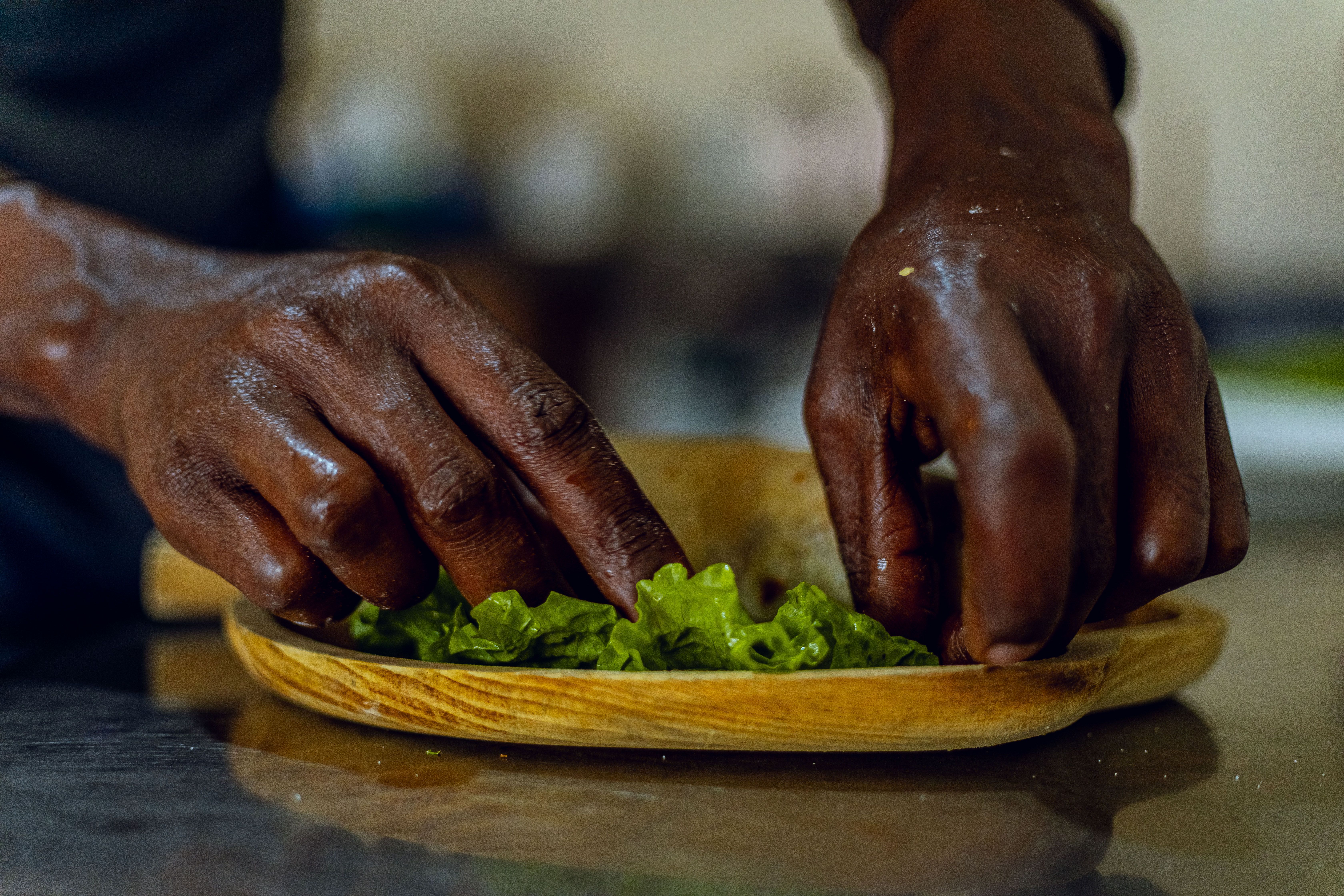 A person arranging fresh green lettuce on a wooden plate in a kitchen setting.
