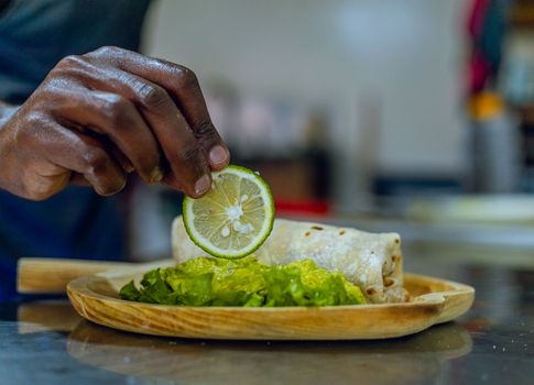 Close-up of a hand garnishing a burrito with lime slice in a kitchen. Perfect for food and culinary themes.