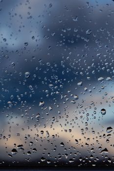Raindrops on a window with a moody cloudy sky in the background, creating a dramatic atmosphere.